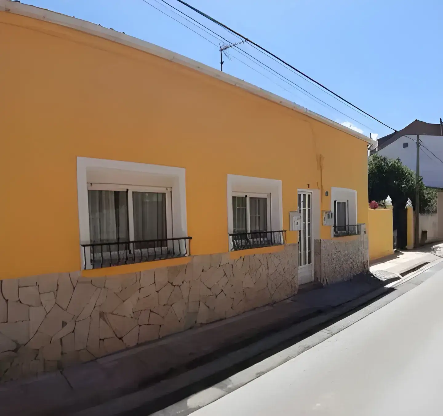 Los Pintores Toledo pintan fachada de casa tradicional pintada en color amarillo con zócalo de piedra